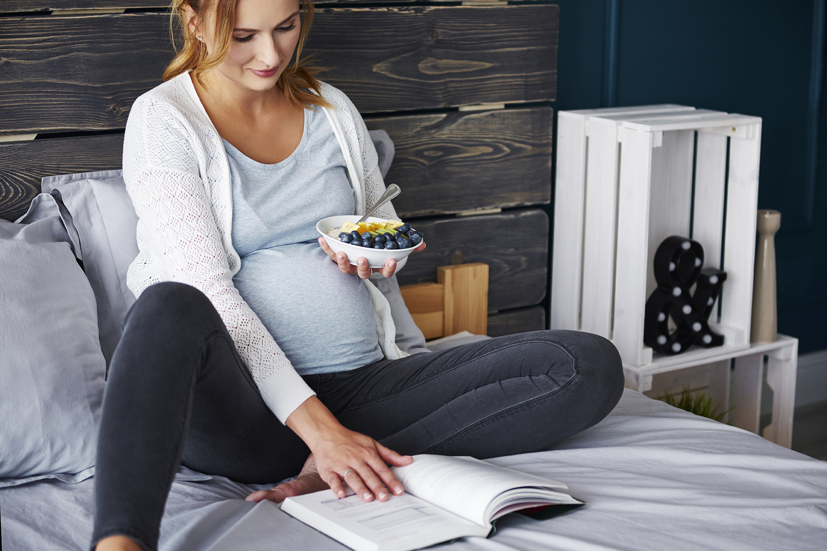 Mujer embarazada comiendo mientras lee un libro
